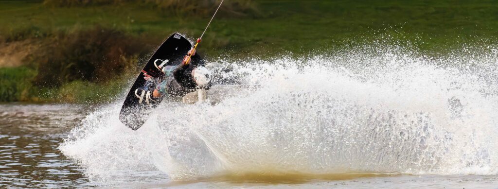 Wakeboarder réalisant une figure spectaculaire avec des éclaboussures d'eau au Wake Park de la Rincerie, situé en Mayenne.